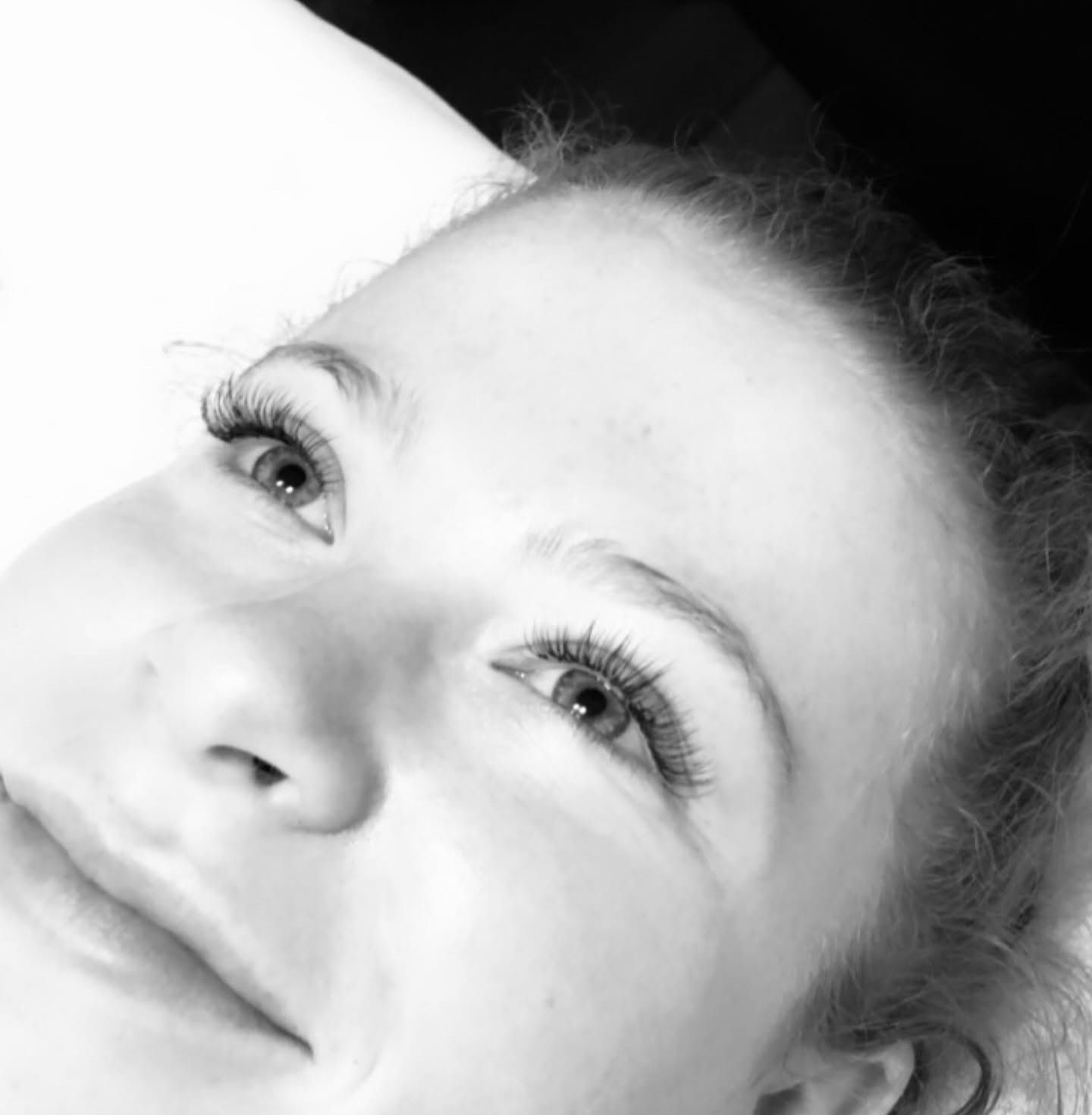 A client lying back and smiling, with lash extensions, in black and white