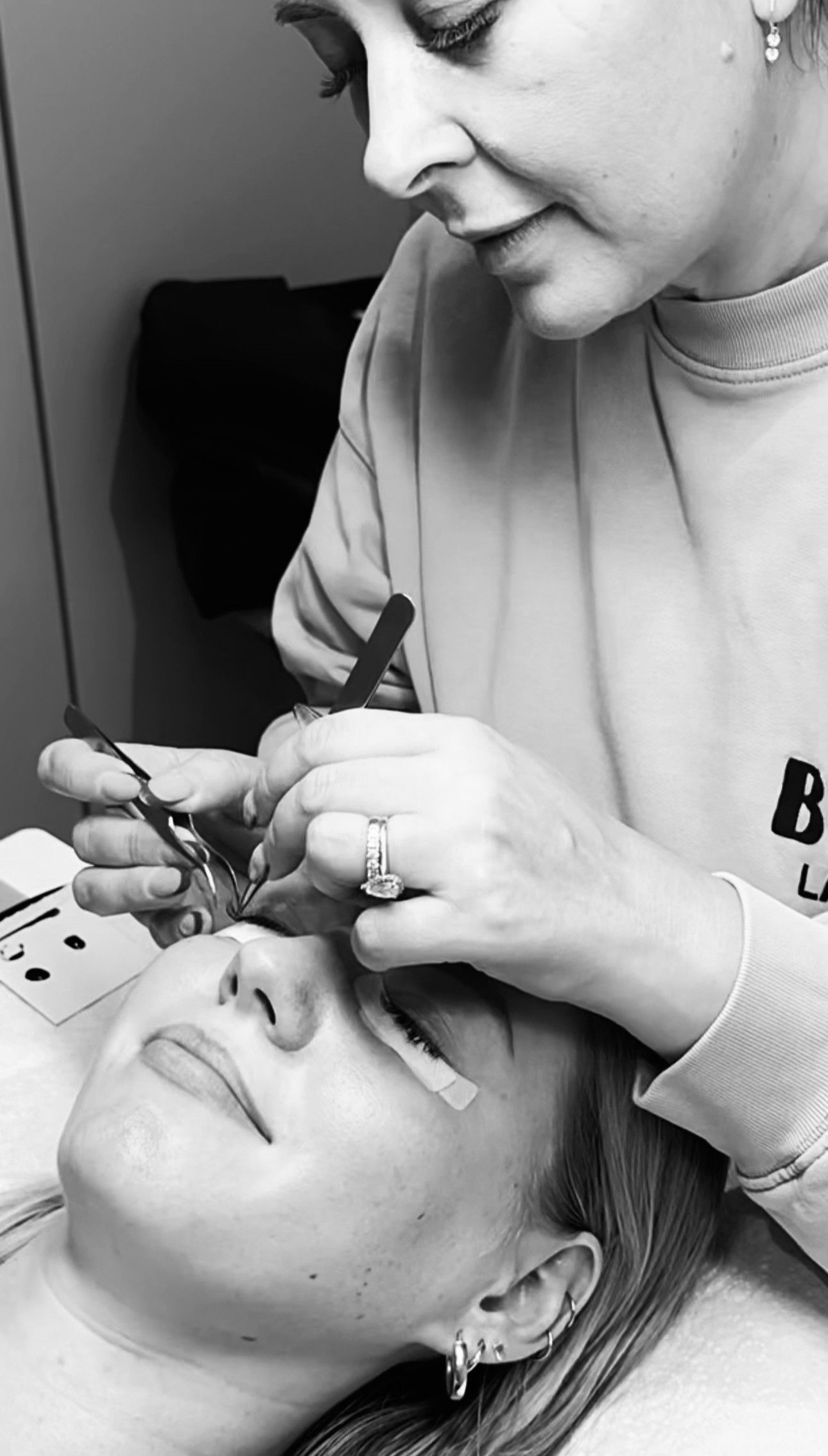 Jess applying lash extensions for a client, in black and white