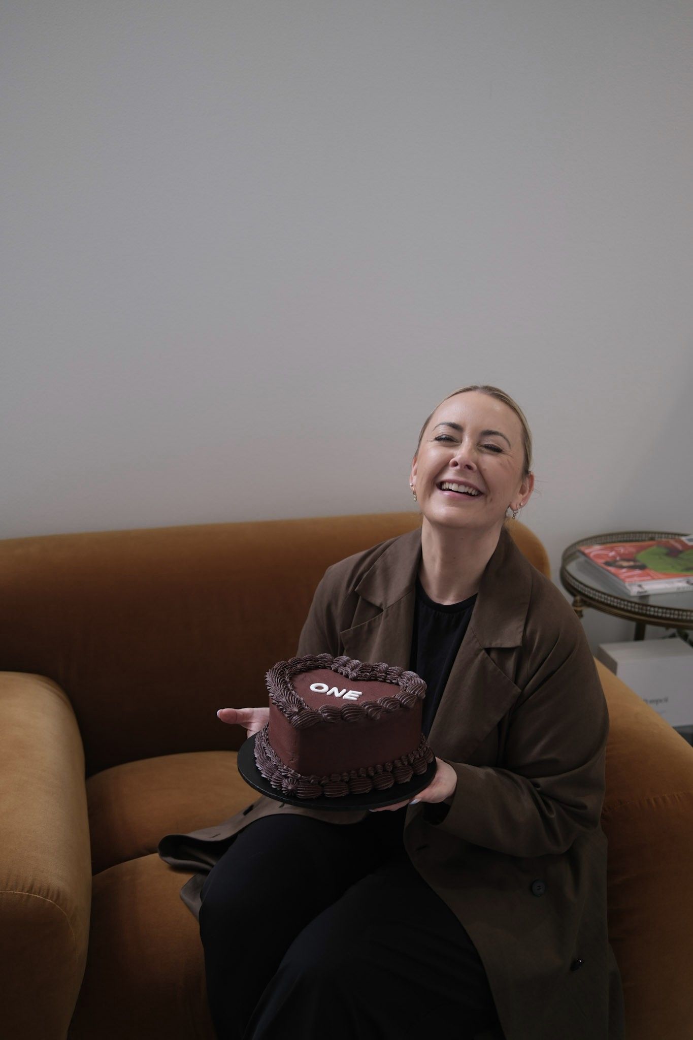 Jess laughing on a velvet sofa, holding a heart-shaped chocolate cake