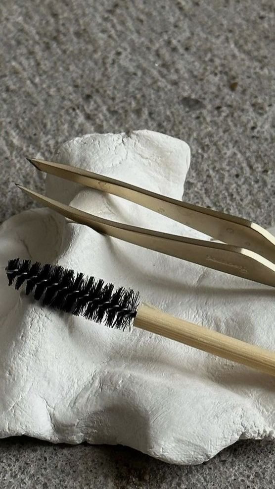 Gold tweezers and a bamboo spoolie on white plaster